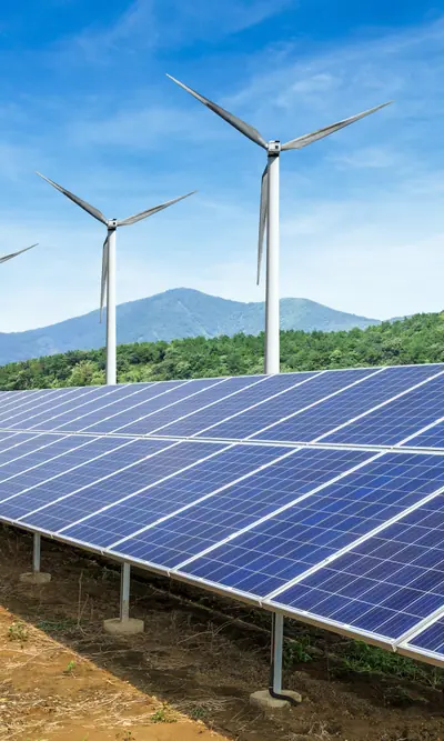 Solarpark mit Photovoltaikmodulen und Windkraftanlagen vor bewaldeten Bergen